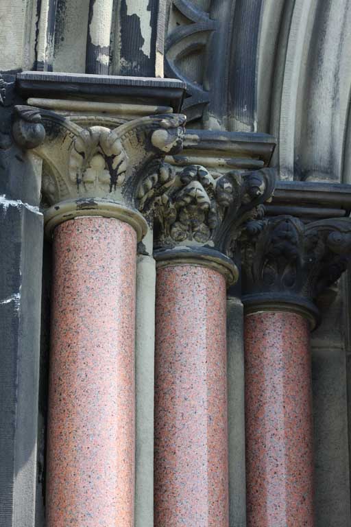Colour photograph of tops of three red columns at entrance to stone building