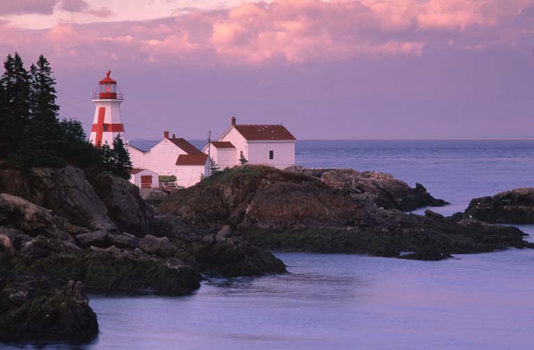 Colour photograph of rocky coastline and ocean with red and white lighthouse