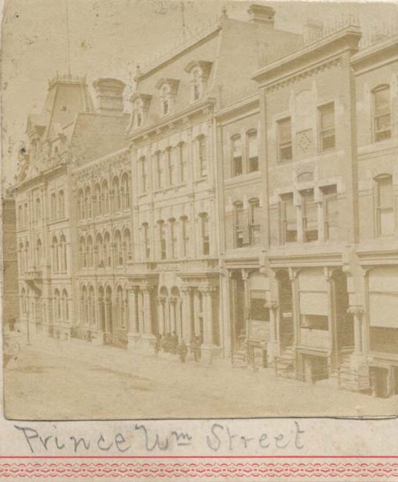 Photographie noir et blanc d’une rue, de devantures de magasins et d’immeubles en pierre