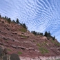 Colour photograph of a cliff of red rocks and a blue sky with clouds