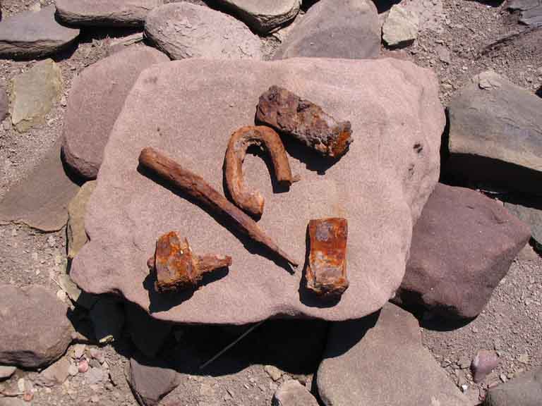 Colour photograph of a red rock with five small rusty tools on it