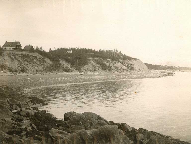 Black and white photograph of a shoreline with high cliffs and a house on top