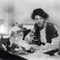 Black and white photograph of a women sitting at a old fashioned microscope